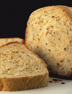 Whole grain bread loaf with sliced pieces on a white surface, against a black background.