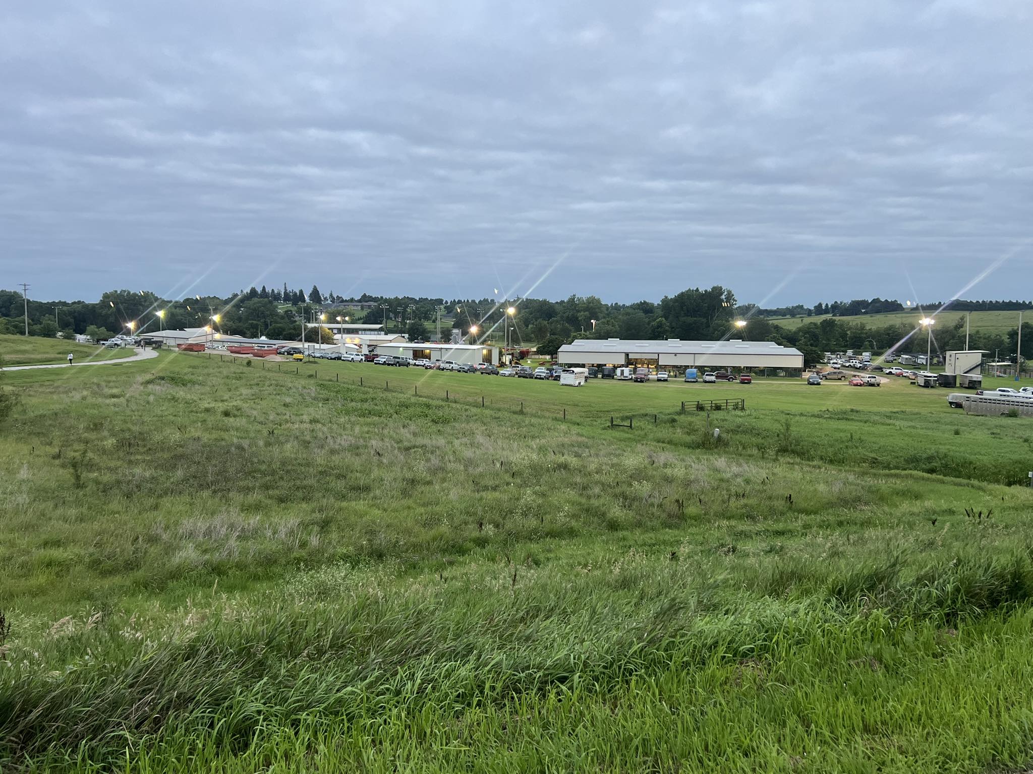 Buildings with bright lights on grassy land under a cloudy sky.