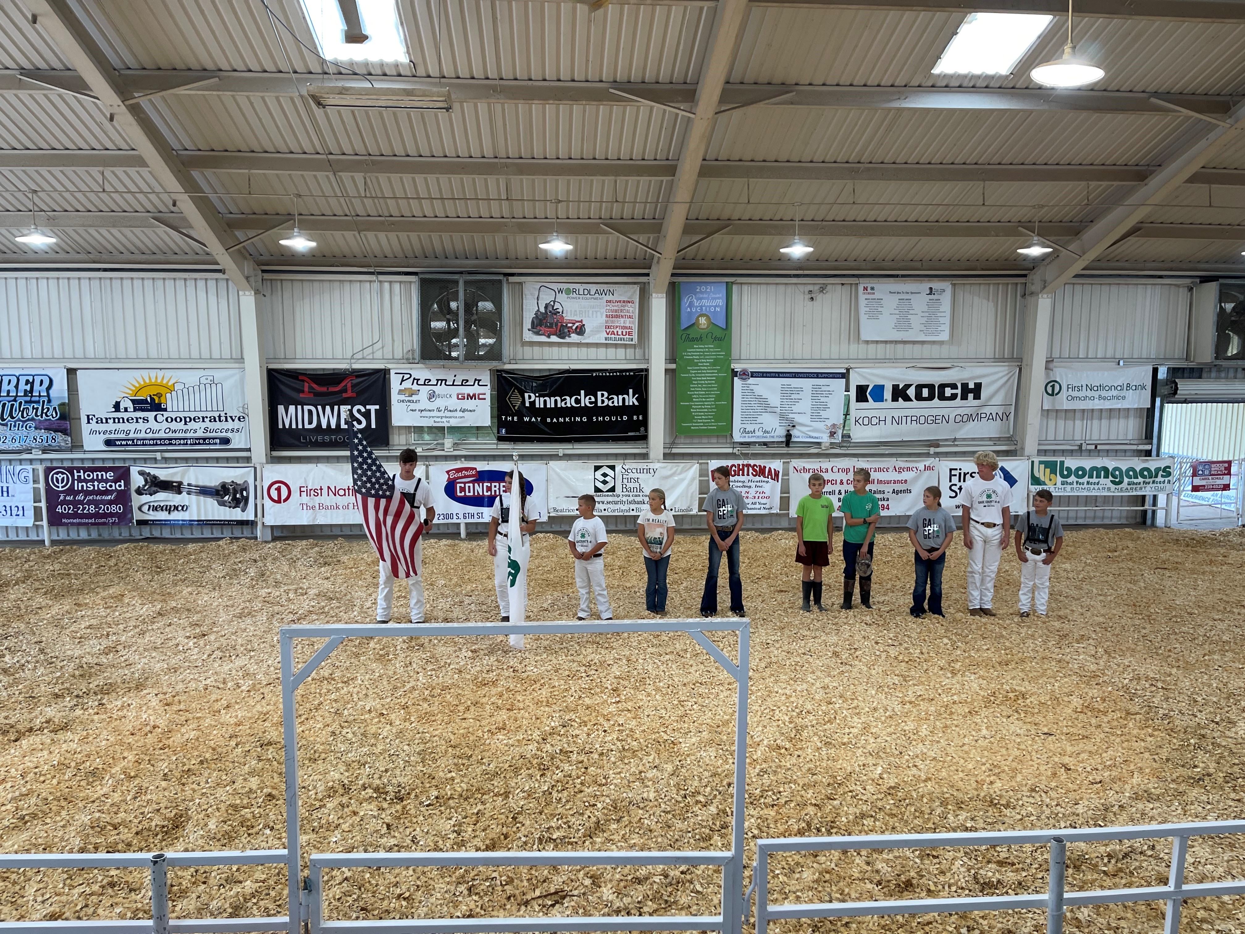 Gage County 4-H Club holding U.S. Flag and 4-H Flag in Show Arena with sponsor banners in the background