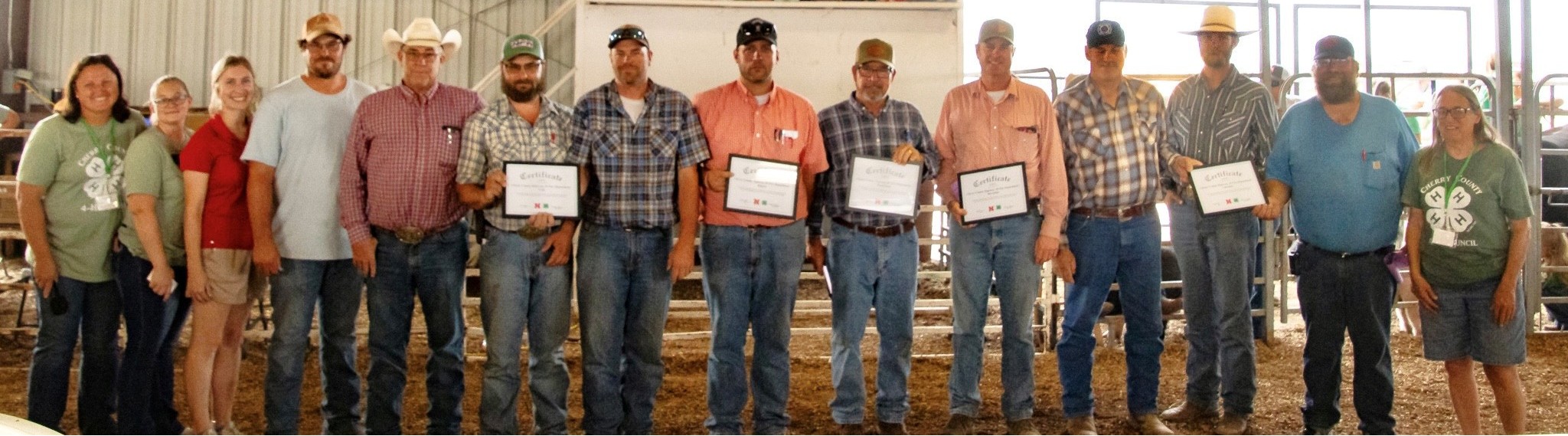 A group of people standing in a row indoors, some holding certificates, wearing casual and cowboy attire.