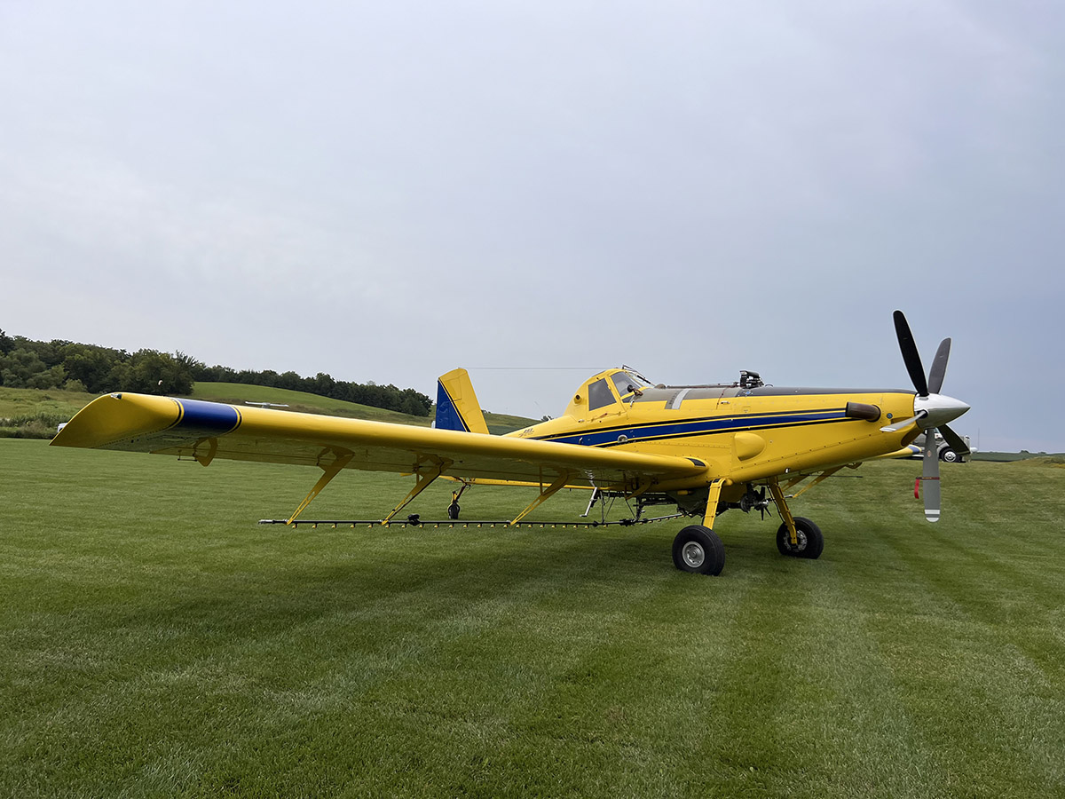 Yellow crop duster airplane parked on a grassy field under a cloudy sky.
