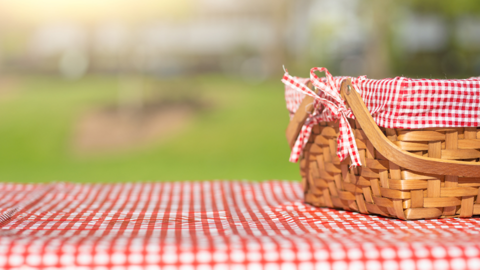 Picnic basket on a picnic table with red and white checkered table cover