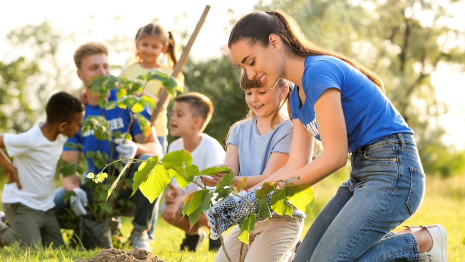 A club leader plants trees with five 4-H club members