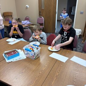 youth making pizza on a brown table in a room of the library