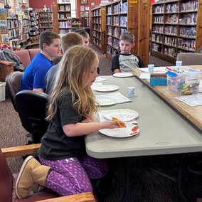 group of youth at a table in the library eating pizza