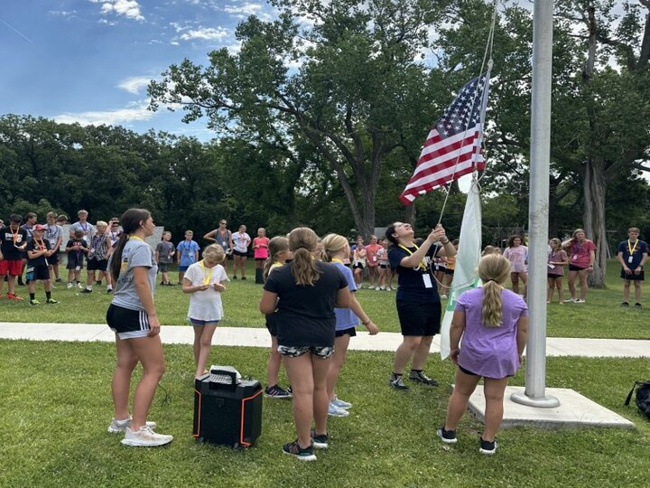 Youth gathered around a flag pole. One youth raising American flag and 4-H flag