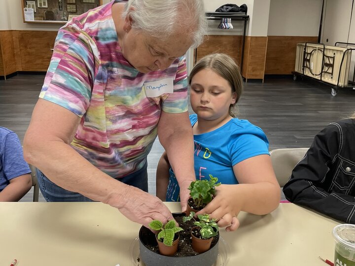 A helper assists a 4-H member in creating their fairy garden at a workshop for homeschooled youth.