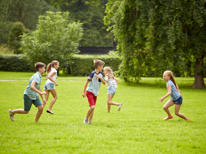 Children running and playing on lush green grass in a park surrounded by trees.