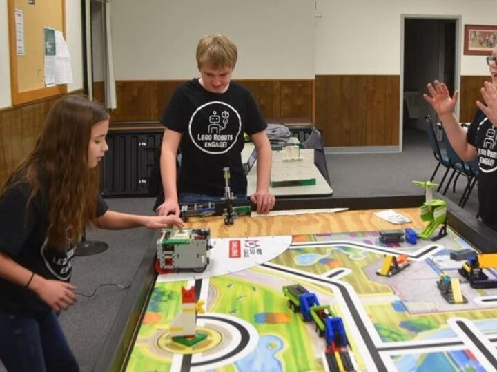 Two boys, one girl practicing robotics around a table with course outlined on top.