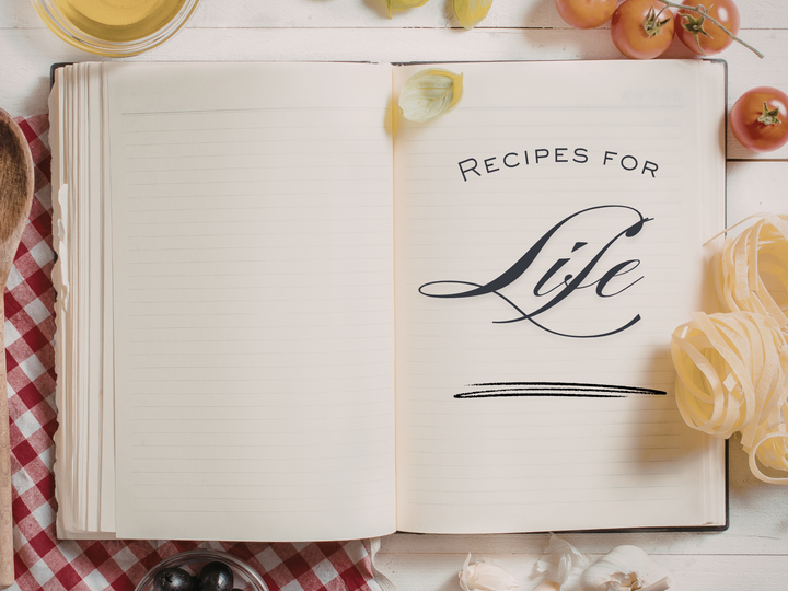 Open cookbook with "Recipes for Life" text, surrounded by pasta, tomatoes, garlic, and olive oil.