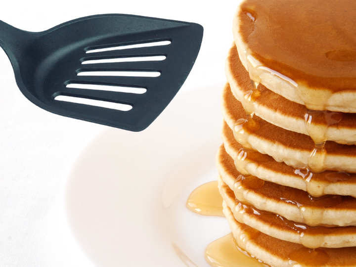 Stack of pancakes with syrup next to a black spatula.