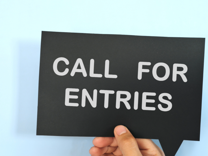 Blue background hand holding a black sign that says "Call for Entries"
