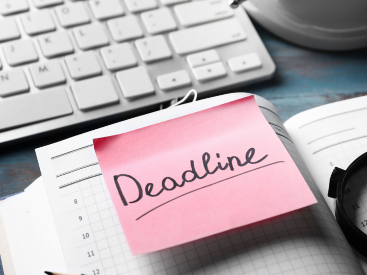 Pink sticky note with "Deadline" on an open planner, near a keyboard and clock.