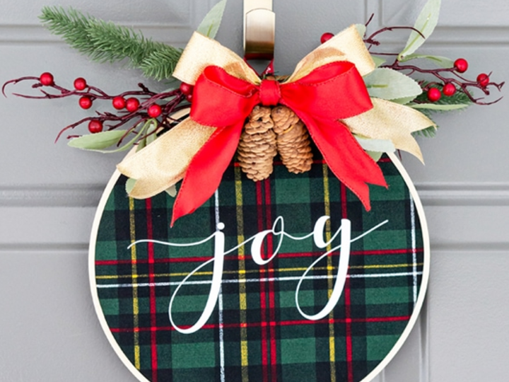 Plaid round sign with "joy," red berries, pinecones, greenery, gold and red ribbon.
