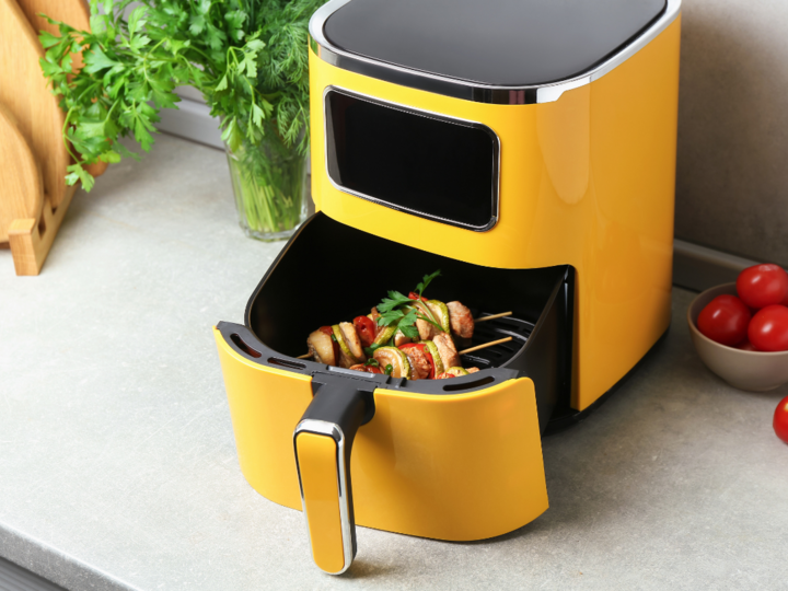 Yellow air fryer with drawer partially pulled out to reveal a meal of kabobs.