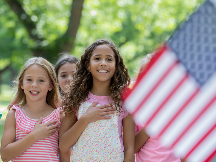 Three young girls looking toward American flag with hand on heart saying pledge 