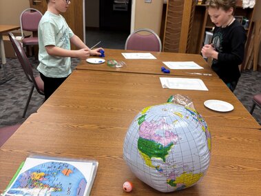 Library setting two youth learning about our world with a globe and a picture of the world on the brown table