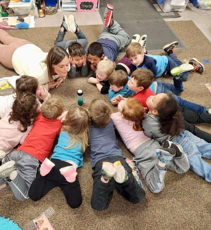 Teacher and Children lying on the floor in a circle, learning meditation by focusing on a glitter bottle in the center of the circle