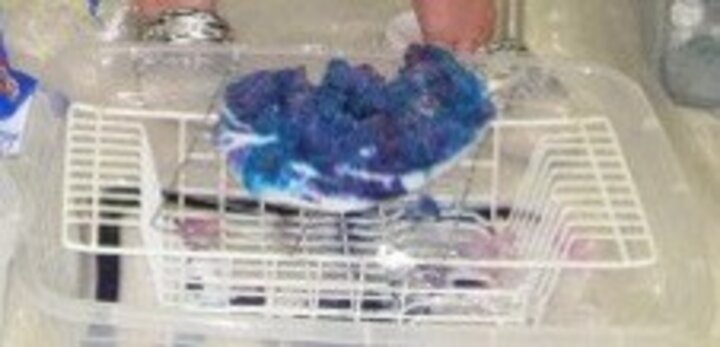 Purple and blue crystal cluster drying on a wire rack above a plastic container.