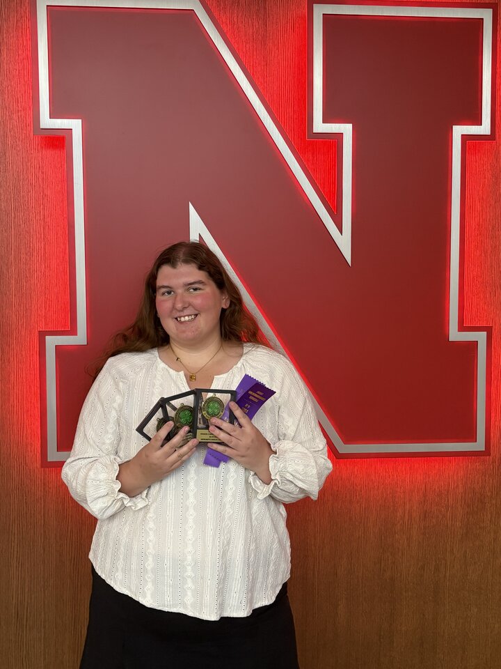 Woman holding cards, standing in front of a large, illuminated red letter "N" on a wood-paneled wall.