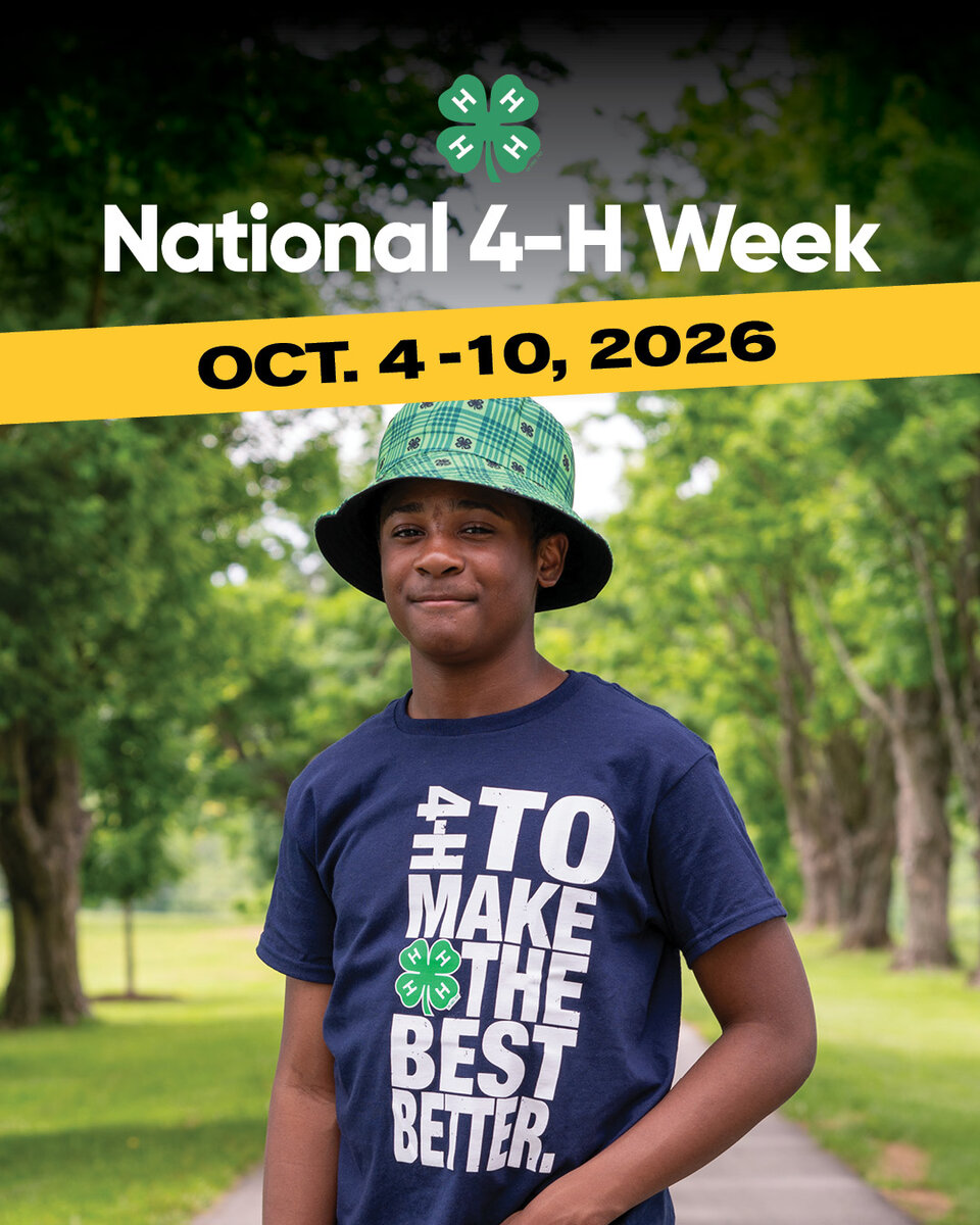 Teen boy in a green 4-H hat and blue shirt stands on a tree-lined pathway outdoors.